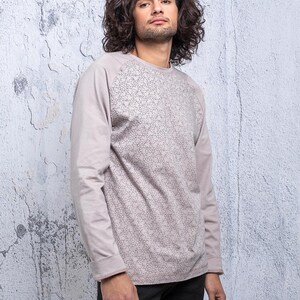 May include: A long-sleeved shirt with a light gray color and a patterned design. The shirt has a raglan sleeve style.