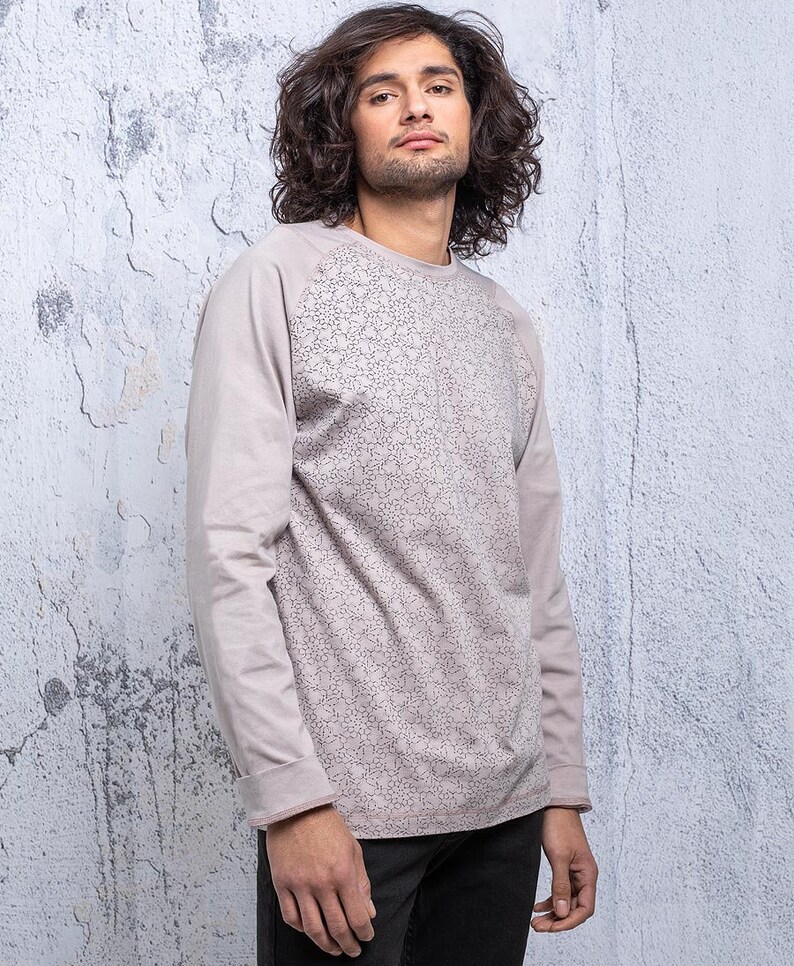 May include: A long-sleeved shirt with a light gray color and a patterned design. The shirt has a raglan sleeve style.