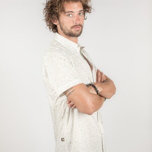 May include: A white short-sleeved button-down shirt with a small, all-over print. The shirt has a relaxed fit and a collar.