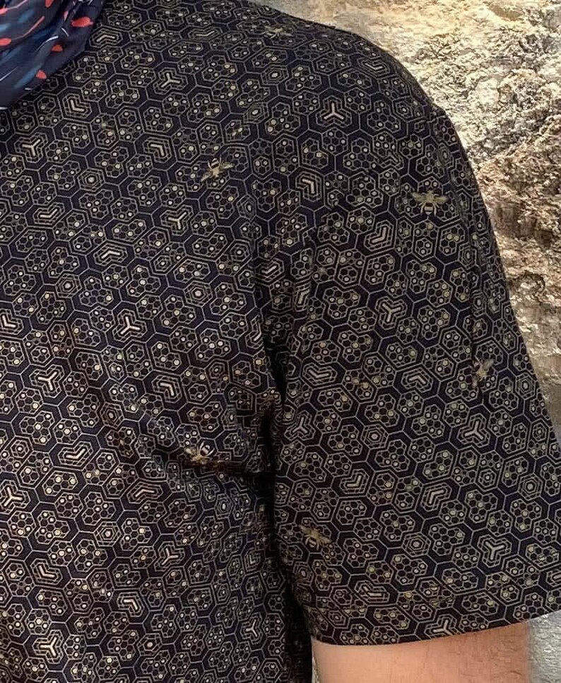 Puede incluir: Una camisa negra de manga corta con un patr&oacute;n geom&eacute;trico dorado de hex&aacute;gonos y l&iacute;neas. El patr&oacute;n se repite en toda la camisa.