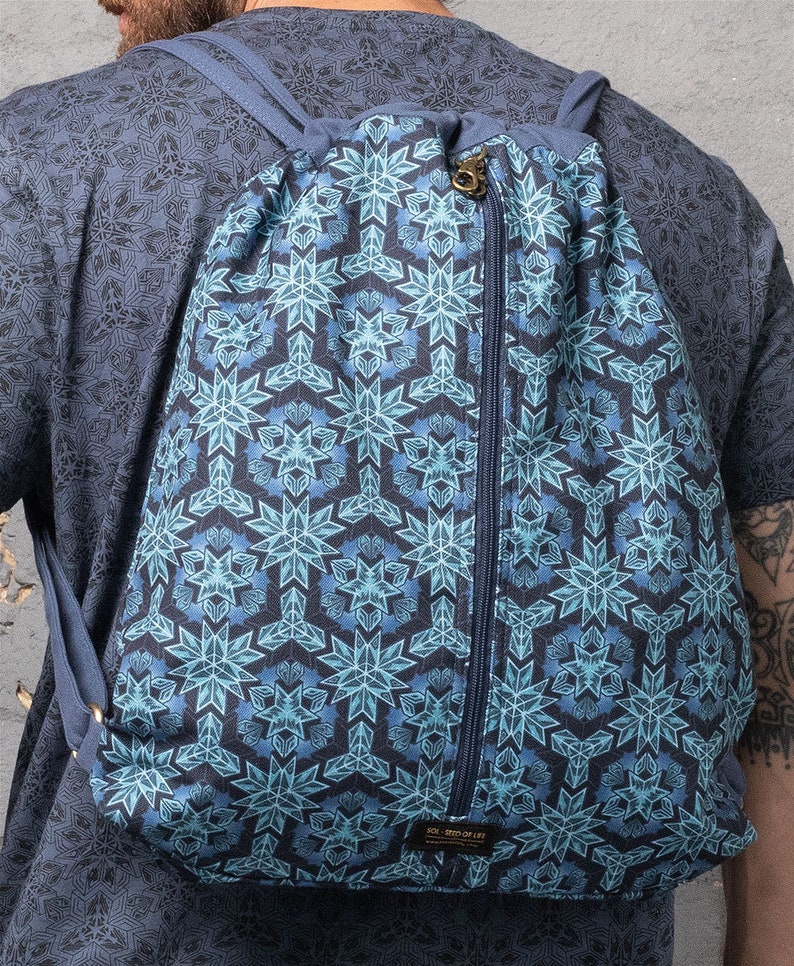 Puede incluir: Una mochila azul de cord&oacute;n con un bolsillo con cremallera y un patr&oacute;n geom&eacute;trico de copo de nieve. La mochila tiene correas ajustables y una peque&ntilde;a etiqueta que dice "SOL SEED OF LIFE".