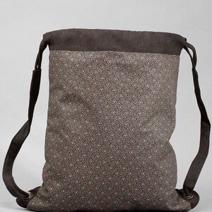 May include: A brown drawstring backpack with a patterned design. The main body of the bag features a repeating pattern of small triangles in shades of brown, black, and orange. The top and straps are a solid dark brown.