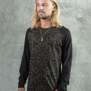 May include: A black long-sleeved shirt with a geometric pattern in gold. The shirt has a crew neck and a raglan sleeve design.