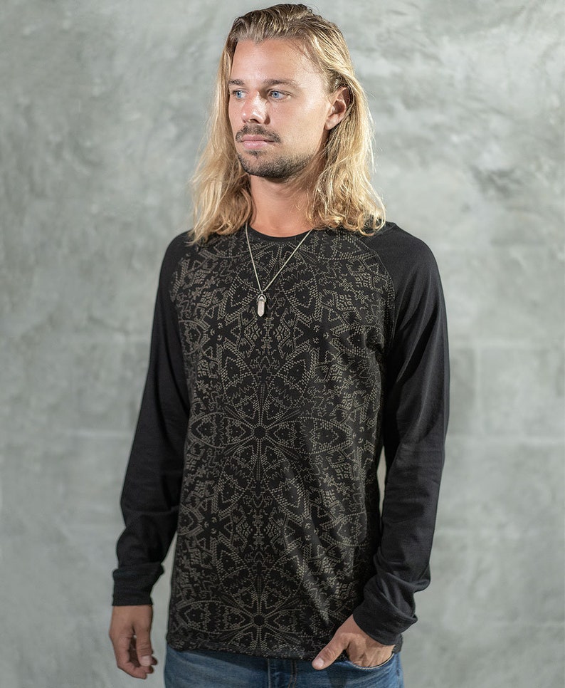 May include: A black long-sleeved shirt with a geometric pattern in gold. The shirt has a crew neck and a raglan sleeve design.
