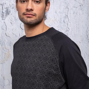 May include: Black long-sleeve shirt with a geometric pattern on the front. The shirt has a raglan sleeve design.