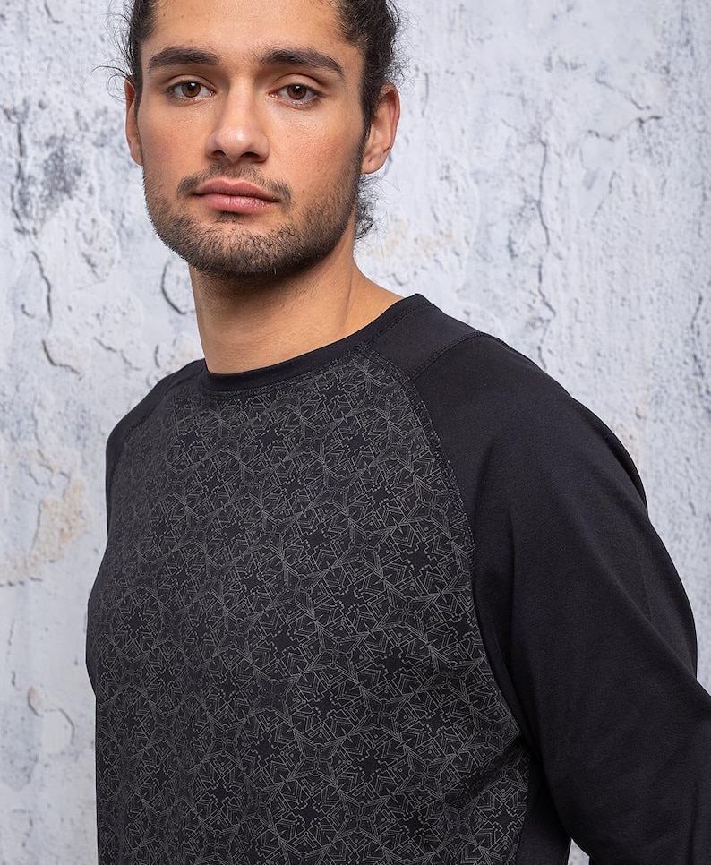 May include: Black long-sleeve shirt with a geometric pattern on the front. The shirt has a raglan sleeve design.