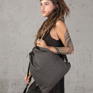 May include: A dark gray drawstring backpack with a repeating pattern of small orange dots. The bag has black straps and metal eyelets. The bag is made of a textured fabric and appears to be worn over the shoulder.