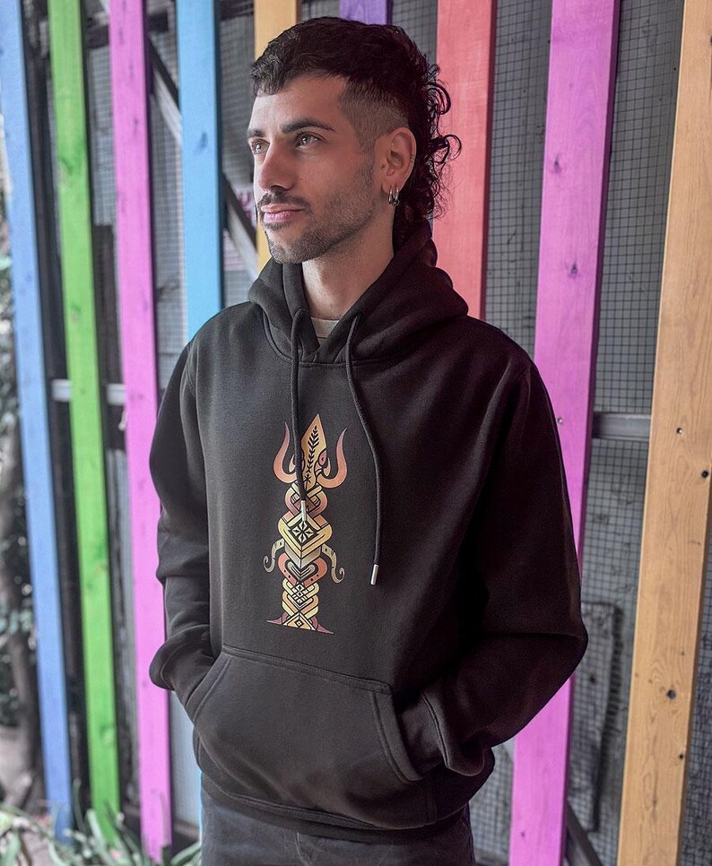 May include: Black hoodie with a front pocket and a hood. The hoodie features a colorful, detailed graphic design on the front. The design is a vertical, symmetrical pattern with orange, yellow, and brown hues.