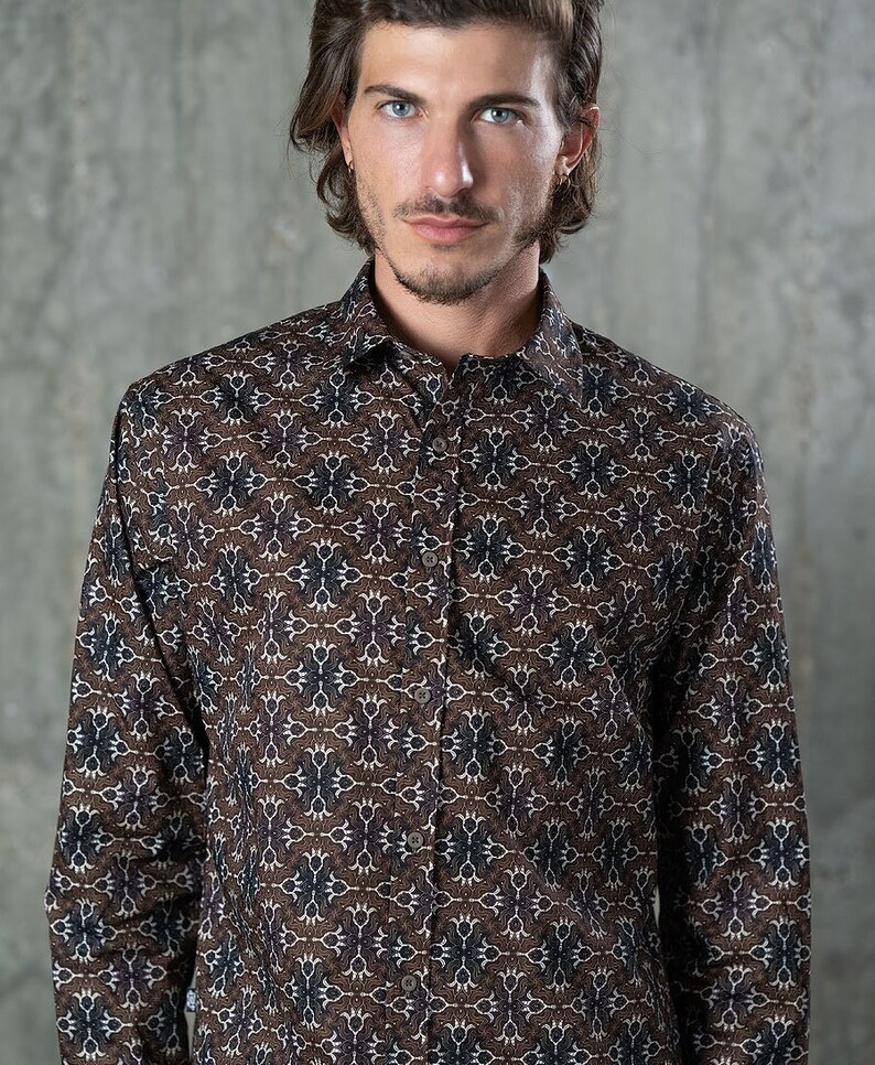 May include: A button-down shirt with a repeating pattern in brown, white, and navy blue. The long-sleeved shirt has a classic collar and is made of a soft, likely woven fabric. The shirt is worn by a person.