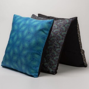 May include: Three decorative throw pillows. One pillow is blue with a subtle pattern, another is black with a paisley pattern, and the third is black with a geometric pattern.