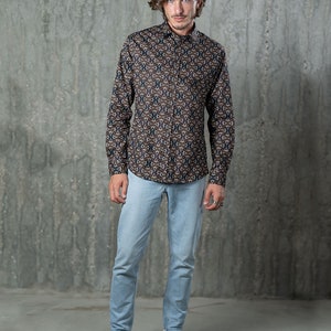 May include: A button-down shirt with a repeating geometric pattern in brown, navy, and white is paired with light blue jeans and white sneakers. The shirt has long sleeves and a classic collar. The jeans are a slim fit.