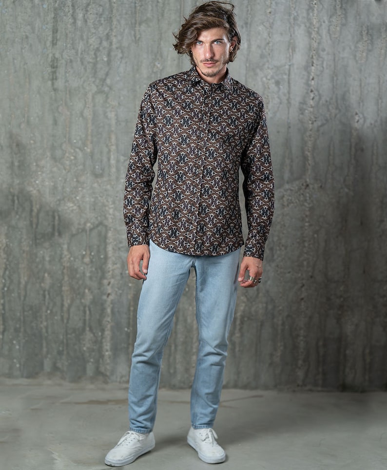May include: A button-down shirt with a repeating geometric pattern in brown, navy, and white is paired with light blue jeans and white sneakers. The shirt has long sleeves and a classic collar. The jeans are a slim fit.