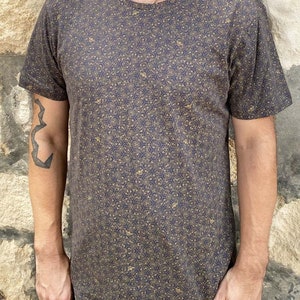 Puede incluir: Una camiseta gris oscura con un patr&oacute;n geom&eacute;trico dorado.
