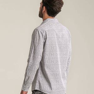May include: A white long-sleeved shirt with a black geometric pattern. The shirt has a button-down collar and a relaxed fit.