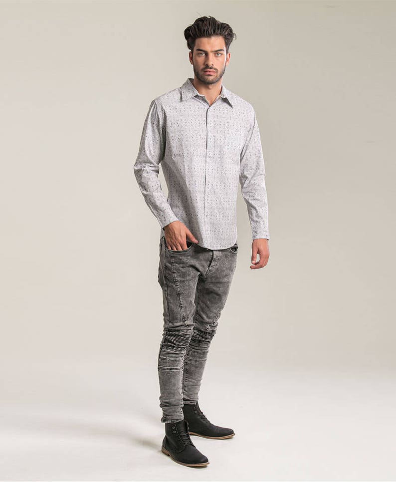 May include: A man wearing a white button-down shirt with a small pattern and dark gray jeans. He is wearing black boots.