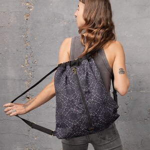 Puede incluir: Una mochila negra de cord&oacute;n con un estampado floral blanco. La mochila tiene una cremallera y correas ajustables.