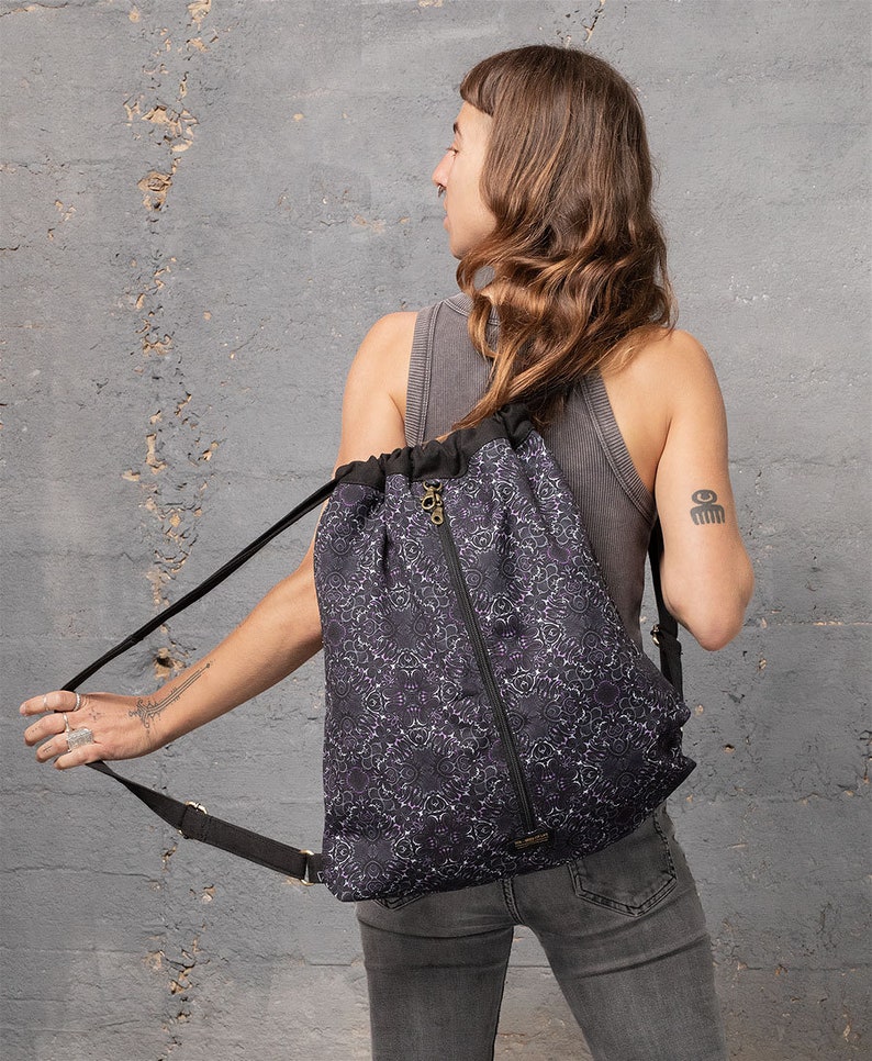 Puede incluir: Una mochila negra de cord&oacute;n con un estampado floral blanco. La mochila tiene una cremallera y correas ajustables.