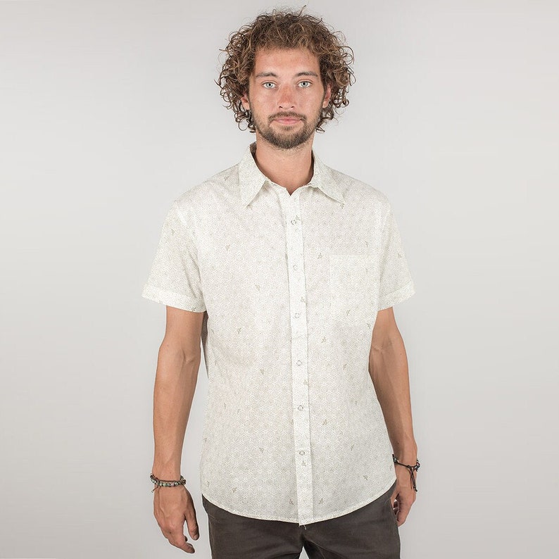 May include: A white short-sleeved button-down shirt with a small, all-over print. The shirt has a classic collar and a chest pocket.