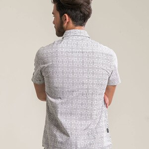 Pode incluir: Uma camisa branca de manga curta com bot&otilde;es e um padr&atilde;o geom&eacute;trico preto.