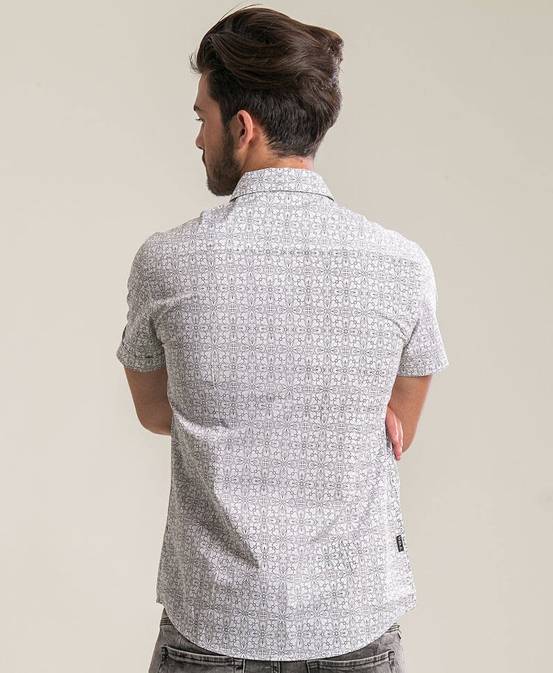 Pode incluir: Uma camisa branca de manga curta com bot&otilde;es e um padr&atilde;o geom&eacute;trico preto.