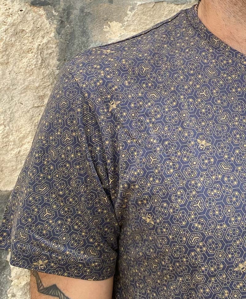 Puede incluir: Una camisa de manga corta azul marino con un patr&oacute;n de panal de abeja dorado y peque&ntilde;as siluetas de abejas.