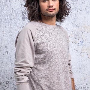 May include: A long-sleeved shirt with a light gray color and a geometric pattern on the front. The shirt has a raglan sleeve design.