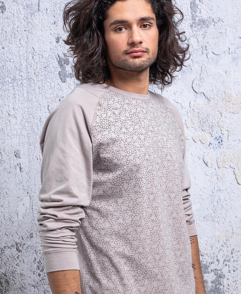 May include: A long-sleeved shirt with a light gray color and a geometric pattern on the front. The shirt has a raglan sleeve design.
