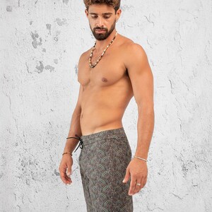 May include: A man wearing a pair of dark green and brown patterned swim trunks with a black drawstring. The trunks have a paisley-like design.