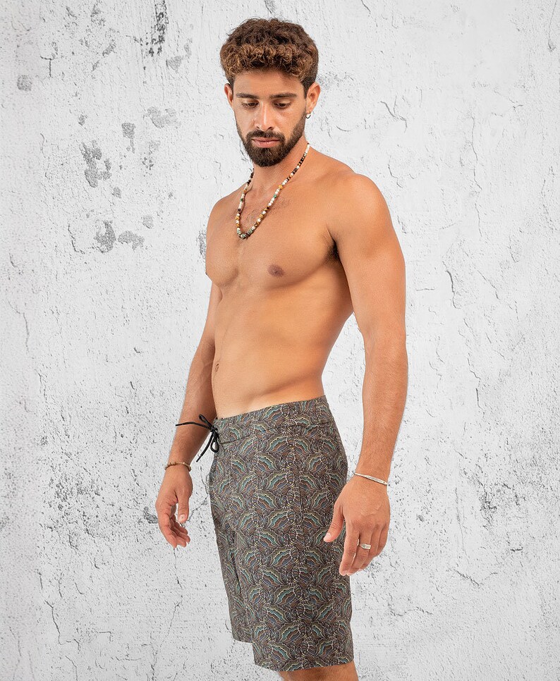 May include: A man wearing a pair of dark green and brown patterned swim trunks with a black drawstring. The trunks have a paisley-like design.