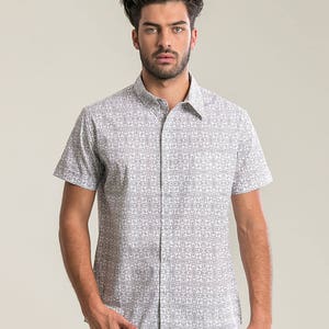 Pode incluir: Uma camisa branca de manga curta com bot&otilde;es e um padr&atilde;o geom&eacute;trico preto.
