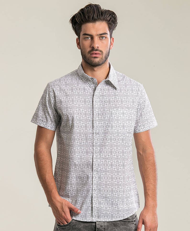 Pode incluir: Uma camisa branca de manga curta com bot&otilde;es e um padr&atilde;o geom&eacute;trico preto.