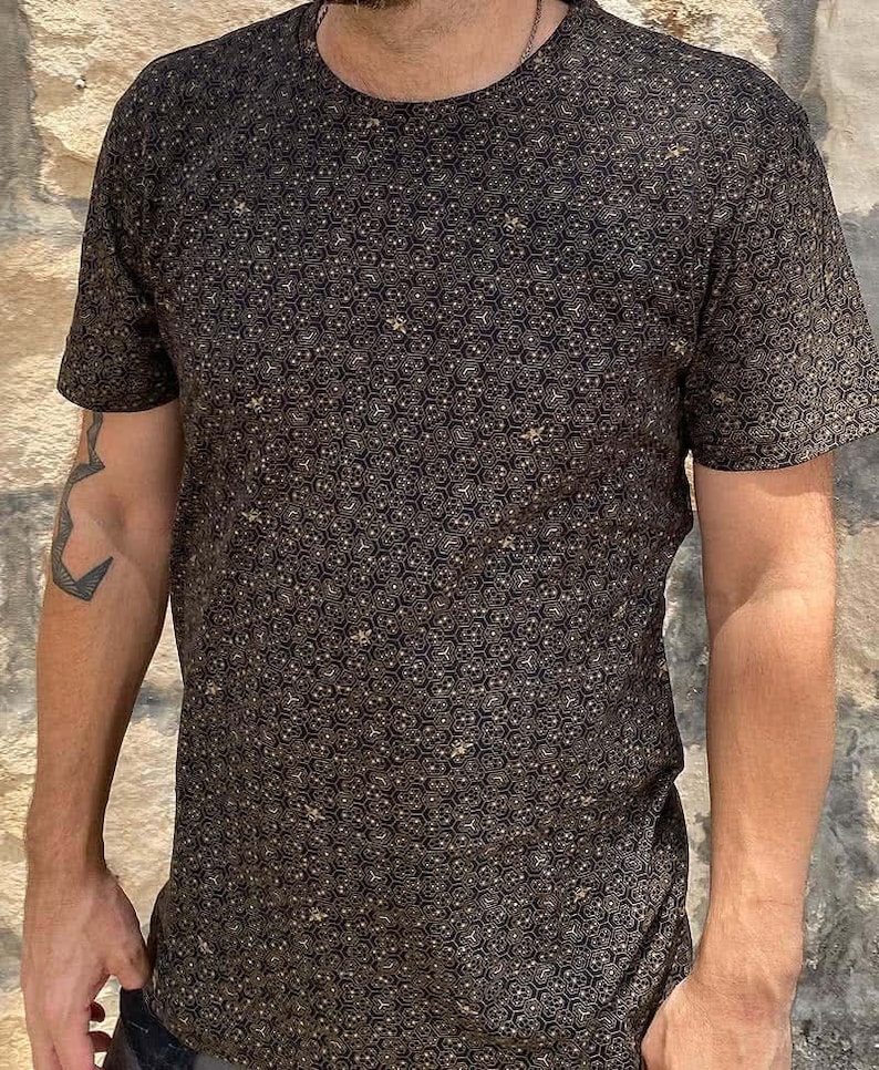 Puede incluir: Una camiseta negra con un patr&oacute;n geom&eacute;trico dorado.