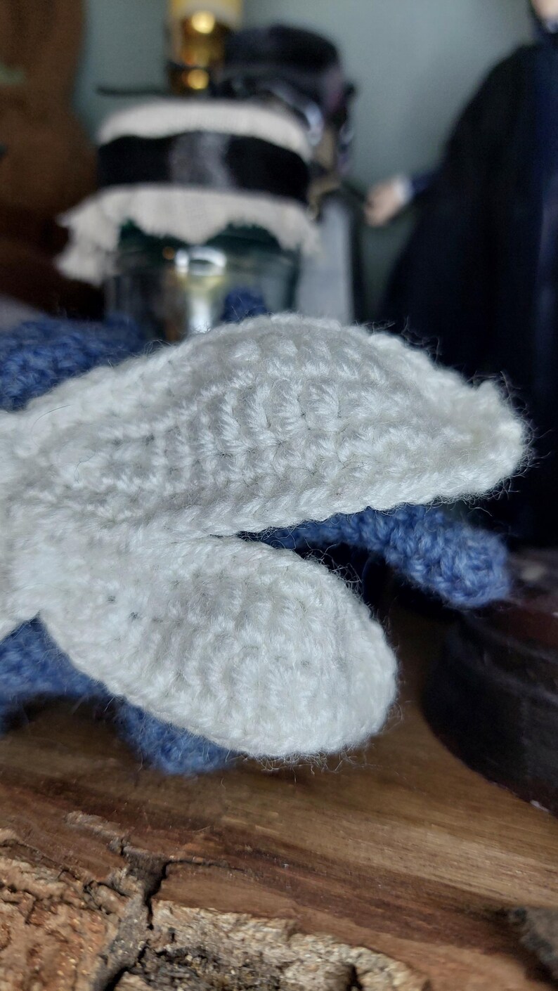 May include: Close-up of a pair of handmade crochet mittens. The mittens feature a white, textured design on the top and a blue base. The mittens are made of soft yarn and appear warm and cozy.