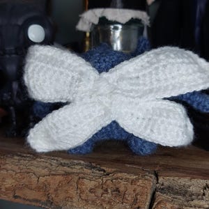 May include: A handmade crochet dragonfly with white wings and a blue body. The wings are large and crossed, and the dragonfly is sitting on a wooden surface. This whimsical item is perfect for home decor or as a unique gift.