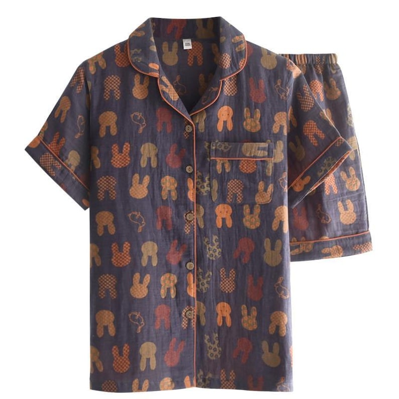 K&ouml;nnte beinhalten: Zweiteiliger Schlafanzug in Marineblau mit einem sich wiederholenden Muster aus orangefarbenen und braunen Hasengesichtern. Das kurz&auml;rmelige Oberteil hat eine Knopfleiste und eine Brusttasche. Die Shorts haben einen elastischen Bund. Orangefarbene Paspeln akzentuieren Kragen, Manschetten und Tasche.