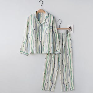 Può includere: Un completo pigiama a due pezzi con un motivo a righe bianche, blu e verdi. La camicia abbottonata a maniche lunghe e i pantaloni presentano un motivo a stelle. Il pigiama è appeso a una gruccia di legno.