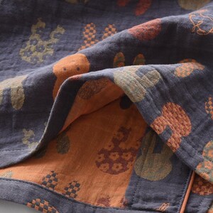 K&ouml;nnte beinhalten: Nahaufnahme eines gefalteten Stoffes mit dunkelblauem Au&szlig;en- und orangefarbenem Innenbereich. Der Stoff ist mit verschiedenen Formen in Orange, Gr&uuml;n und Braun gemustert. Der Stoff scheint weich und strukturiert zu sein, m&ouml;glicherweise Baumwolle oder Leinen.