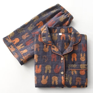 K&ouml;nnte beinhalten: Dunkelgraues Pyjama-Set mit einem sich wiederholenden Muster aus orangefarbenen, braunen und beigen Hasensilhouetten. Das Set beinhaltet ein Hemd mit Kn&ouml;pfen und orangefarbenem Besatz sowie eine passende Hose mit elastischem Bund.