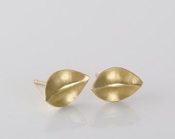 May include: A pair of gold leaf-shaped stud earrings. The earrings are made of a smooth, textured metal and have a subtle shine.