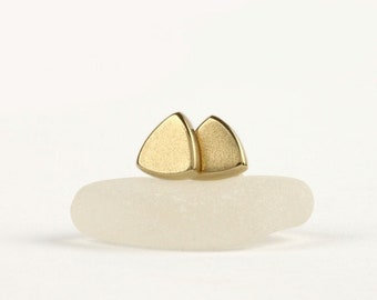 May include: A pair of gold triangle stud earrings. The earrings are small and delicate, and they have a brushed finish.