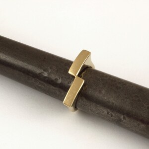 May include: A gold ring with a unique geometric design. The ring is made of two intersecting rectangular shapes, creating a modern and minimalist look.