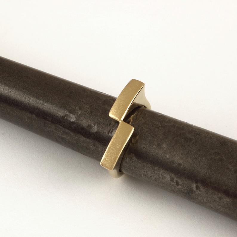 May include: A gold ring with a unique geometric design. The ring is made of two intersecting rectangular shapes, creating a modern and minimalist look.