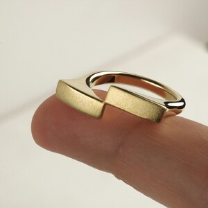 May include: A gold ring with a unique, angular design. The ring is made of a smooth, brushed metal and has a simple, modern aesthetic.