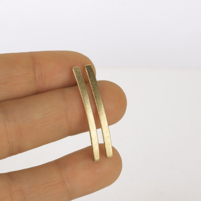 May include: A pair of gold-toned bar earrings. The earrings are long and thin, with a slightly curved shape.