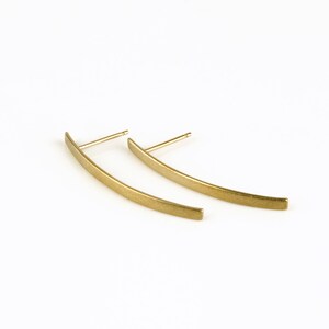May include: A pair of gold-toned curved bar earrings. The earrings are made of a smooth, brushed metal.