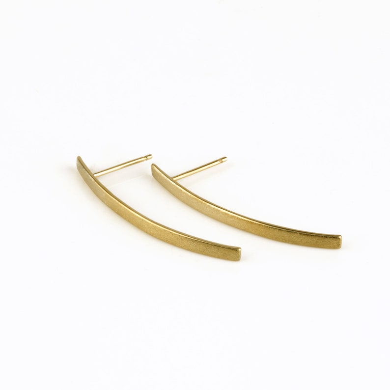 May include: A pair of gold-toned curved bar earrings. The earrings are made of a smooth, brushed metal.