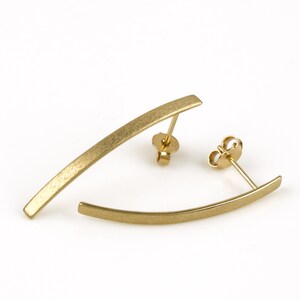 May include: A pair of gold-toned earrings with a curved bar design. The earrings have a brushed finish.