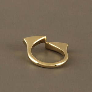 May include: A gold-colored ring with a unique, abstract design. The ring is made of two pieces that are joined together in the middle, creating a split-ring effect.