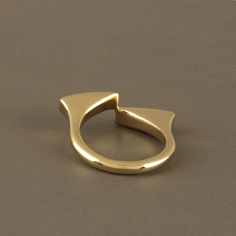 May include: A gold-colored ring with a unique, abstract design. The ring is made of two pieces that are joined together in the middle, creating a split-ring effect.