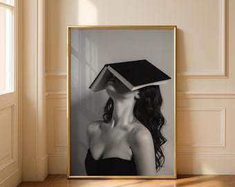 Op de afbeelding: Zwart-wit ingelijste kunstafdruk. De afbeelding toont een persoon met lang, donker haar en een zwart boek dat hun gezicht bedekt. De persoon draagt een zwarte strapless top. De lijst is goudkleurig.
